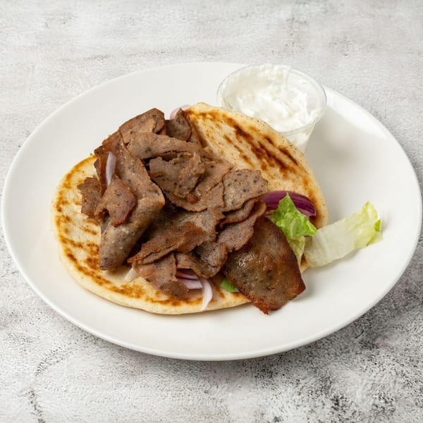 Gyro meat, red onion, and lettuce on pita bread with a side of tzatziki sauce.