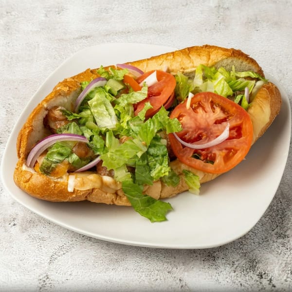 A large sub sandwich with chicken, melted cheese, lettuce, tomatoes, and red onions on a white plate.