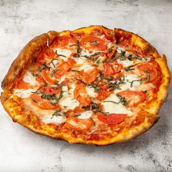 A whole Margherita pizza with sliced tomatoes, mozzarella, and basil on a light gray surface.